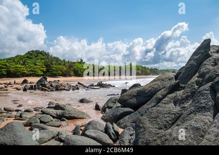 Schwarze dunkle Felsbrocken liegen an einem Strand nach der Küste in Axim Ghana Westafrika Stockfoto