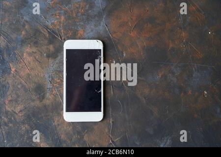 Weißes Telefon mit einem defekten Bildschirm auf dunklem Hintergrund Stockfoto