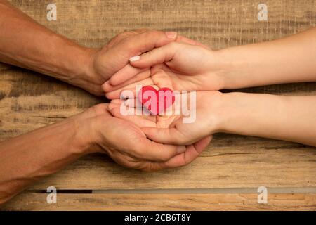 Menschliche Hände halten, geben Herz isoliert auf hölzernen Hintergrund. Konzept der Emotionen, Gefühle, Nächstenliebe, Familie, unterstützende Hand. Dankbar, inspirierend. Romantisch und Zweisamkeit. Stockfoto