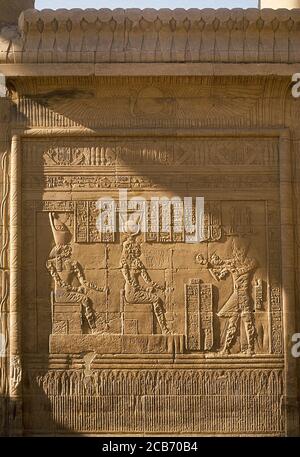 Ägypten, Philae. Reliefs an einer Wand des Tempels von Isis. Darbietszene dem gott Horus (Falkenköpfchen) und der Göttin Isis (Sonnenschale). Unterer Streifen, der Lotusblumen darstellt. Stockfoto