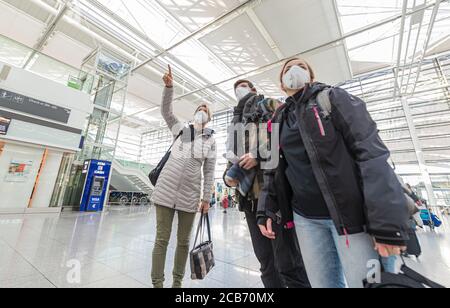 Familie am Flughafen München mit Schutzmaske auf der Suche nach Flüge Stockfoto