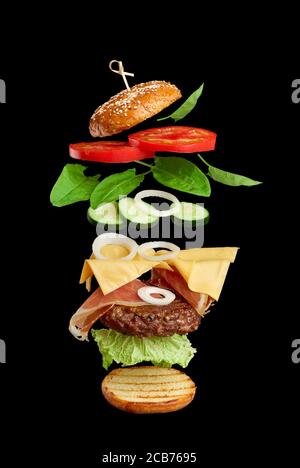 Flying Burger Zutaten: Cutlet, Sesambrötchen, Tomaten, Zwiebeln, grüner Salat, Käse auf schwarzem Hintergrund, leckere Cheeseburger, Sandwichschichten Stockfoto