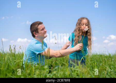 Vater und Töchter verbringen Zeit. Papa und Töchter spielen zusammen auf dem Feld grünen Gras im Sommer. Mädchen weht auf Löwenzahn Stockfoto