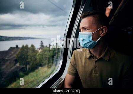 Mann trägt Gesichtsmaske im Zug. Themen New Normal, Coronavirus und Personenschutz im öffentlichen Verkehr. Stockfoto