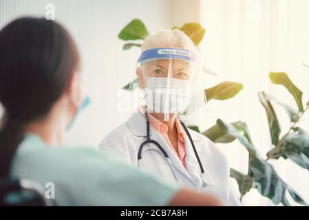 Porträt einer älteren Frau Arzt trägt Gesichtsschutz und Beratung mit Frauen Patienten im Zimmer im Krankenhaus. Gesundheitskonzept Stockfoto