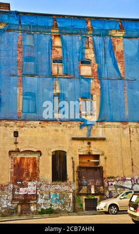 Die Fassade eines alten ruinösen Gebäudes ist mit verkrümmelt Einige blaue Vorhänge, um die Fußgänger zu schützen Stockfoto