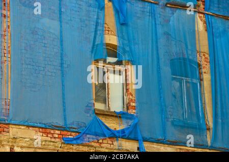 Die Fassade eines alten ruinösen Gebäudes ist mit verkrümmelt Einige blaue Vorhänge, um die Fußgänger zu schützen Stockfoto