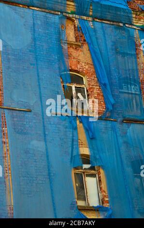 Die Fassade eines alten ruinösen Gebäudes ist mit verkrümmelt Einige blaue Vorhänge, um die Fußgänger zu schützen Stockfoto