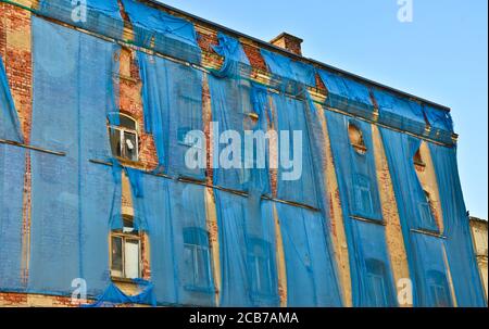 Die Fassade eines alten ruinösen Gebäudes ist mit verkrümmelt Einige blaue Vorhänge, um die Fußgänger zu schützen Stockfoto