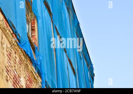 Die Fassade eines alten ruinösen Gebäudes ist mit verkrümmelt Einige blaue Vorhänge, um die Fußgänger zu schützen Stockfoto