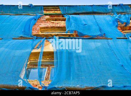 Die Fassade eines alten ruinösen Gebäudes ist mit verkrümmelt Einige blaue Vorhänge, um die Fußgänger zu schützen Stockfoto