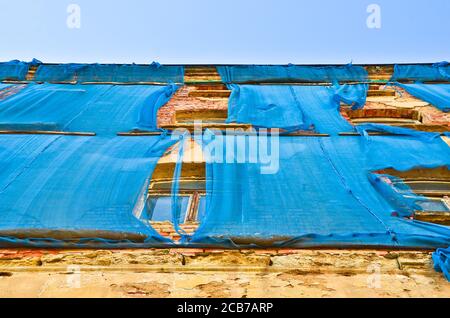 Die Fassade eines alten ruinösen Gebäudes ist mit verkrümmelt Einige blaue Vorhänge, um die Fußgänger zu schützen Stockfoto