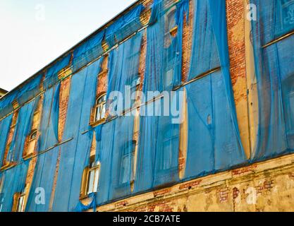 Die Fassade eines alten ruinösen Gebäudes ist mit verkrümmelt Einige blaue Vorhänge, um die Fußgänger zu schützen Stockfoto