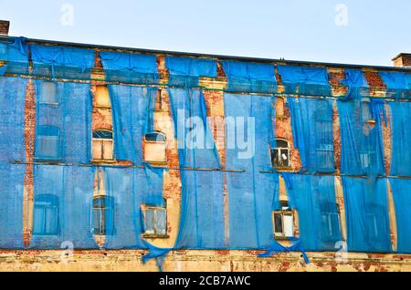 Die Fassade eines alten ruinösen Gebäudes ist mit verkrümmelt Einige blaue Vorhänge, um die Fußgänger zu schützen Stockfoto