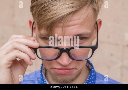 Blonde Mann mit kleinem Bart zieht seine Brille in Überraschung.Junge Mann mit lustigen Haarschnitt in der Brille Grimasse machen - lustige Gesicht. Emotionen und si Stockfoto