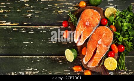 Frische Lachssteaks mit Zitrone, Kirschtomaten und Petersilie auf grünem Holzhintergrund Stockfoto