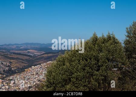 Baumkronen, mit einem üppigen Grün, umrahmt das Tal, wo die Stadt ist, und im Hintergrund Bergkette, meeti Stockfoto