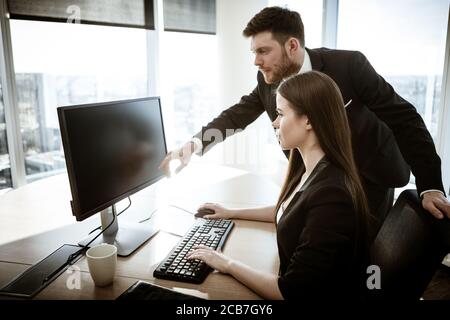 Krisenkonzept. Junge Geschäftsfrau sitzt am Bürotisch beschäftigt am Computer arbeiten. Geschäftsmann zeigt auf Monitor. Lösung eines ernsten Stockfoto