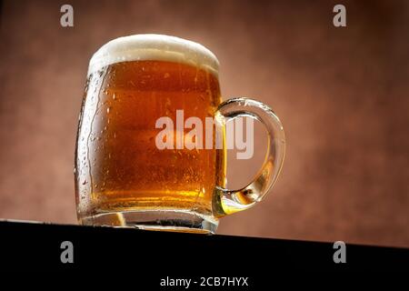 Bierkrug mit Schaum vor braunem Hintergrund Stockfoto