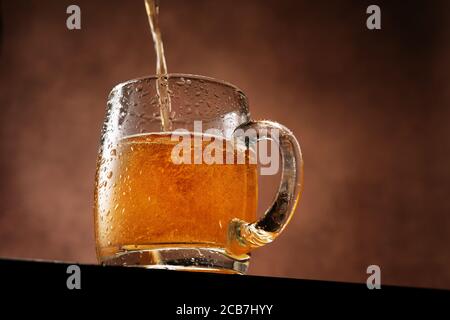 Leichtes Bier wird in einen Becher gegossen, der gegen Braun steht Hintergrund unter der Augenlinie Stockfoto