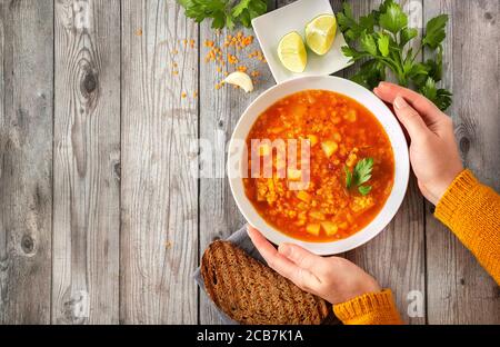 Draufsicht auf die Hände der Frau in Ornage Pullover berühren warm Teller mit Winterlinsensuppe Stockfoto