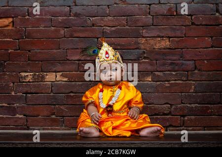 Ein Kind als Lord Krishna gekleidet sitzt außerhalb des Krishna Mandir während des Festivals am Patan Durbar Square.Krishna Janmashtami ist ein jährliches hinduistisches Festival, das die Geburt von Krishna, dem achten Avatar von Vishnu feiert. Es wird nach dem hinduistischen lunisolaren Kalender beobachtet, am achten Tag des Krishna Paksha in Shraavana oder Bhadrapad, der sich mit August oder September des Gregorianischen Kalenders überschneidet. In diesem Jahr wurde aufgrund der anhaltenden Coronavirus (COVID-19) Krise der Eintritt in den Tempel eingeschränkt. Stockfoto