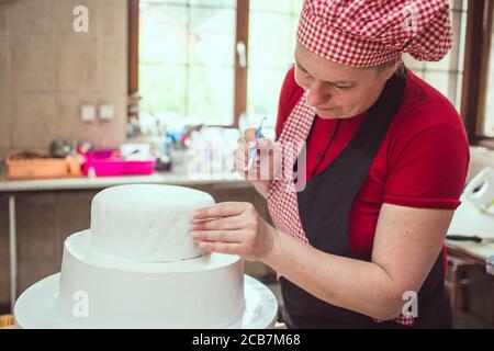 Weibliche Köchin rot Arbeit tragen in pasty Shop Finishing Dekoration auf weißen Fondant Kuchen. Stockfoto