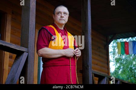 lama Mönch steht auf der Veranda und hält eine hölzerne rosenkranz in seiner Hand Stockfoto