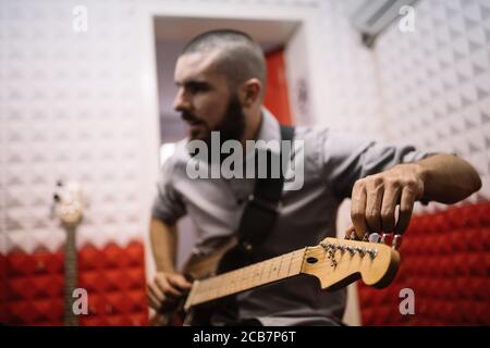 Außer Fokus Gitarrist, der sein Musikinstrument justiert. Verschwommener männlicher Musiker, der seine E-Gitarre stimmt und im Musikstudio sitzt. Stockfoto