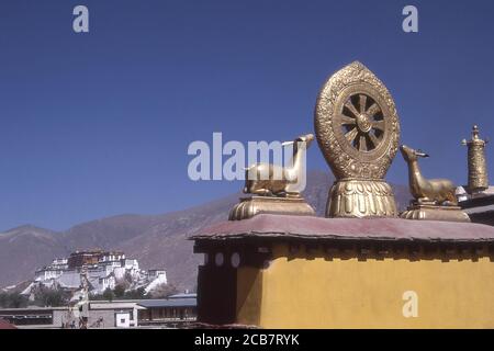 TIBET - DHARMA-RAD UND GOLDENER HIRSCH AUF DEM DACH DES JOKHANG-TEMPELS, LHASA. POTALA PALAST IM HINTERGRUND SICHTBAR. Stockfoto