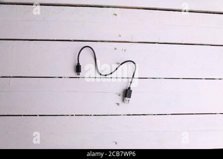 Draufsicht auf ein schwarzes Ladekabel isoliert auf einem Weiße Holzoberfläche Stockfoto