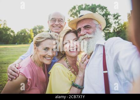 Gruppe von Senioren, die ein Picknick im Park machen und Spaß haben. Selfies mit Freunden aufnehmen Stockfoto