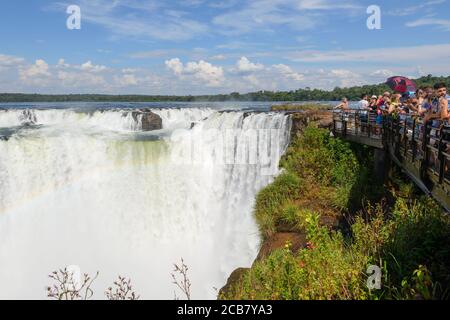 Touristen, die den Teufelskehlchen-Wasserfall in den Iguazu Fällen an der Grenze zu Brasilien und Argentinien vom Iguazu Nationalpark auf der argentinischen Seite besuchen. Stockfoto