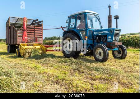 Leap, West Cork, Irland. Juli 2020. An einem heißen Sonnentag sammeln Mitglieder des Leap und des District Vintage Club Silage für Leap Farmer Andrew Whelton mit Vintage-Traktoren und Erntemaschinen. Shane Jennings ist abgebildet, einen Ford 7600 von 1979 zu fahren, der Gras mit einem New Holland 717 aus den 1970er Jahren sammelt. Quelle: AG News/Alamy Live News Stockfoto