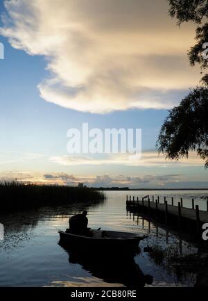 Ein Fischer bereitet sein Boot in der Morgenröte für einen Tag vor Vom Fischen, während die Sonne aufgeht und die Wolken Rollen Zoll Stockfoto