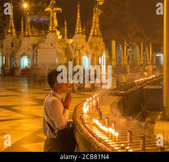 Yangon, Myanmar - 18. Dezember 2017: Ein Mann betet neben einigen Kerzen am Shwedagon Pago in Yangon, Myanmar Stockfoto