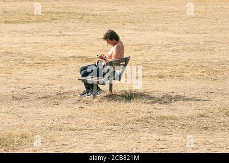 WIMBLEDON LONDON, GROSSBRITANNIEN - 11. AUGUST 2020. Menschen sitzen auf dem ausgetrockneten Gras am späten Nachmittag auf Wimbledon Common verursacht durch minimale Regenfälle in den letzten Monaten und die trockenen Bedingungen durch die aktuelle Hitzewelle gebracht. Die Prognose ist, dass hohe Temperaturen bis Donnerstag bleiben und Gewitter bis zum Ende der Woche Kredit: amer ghazzal/Alamy Live News Stockfoto