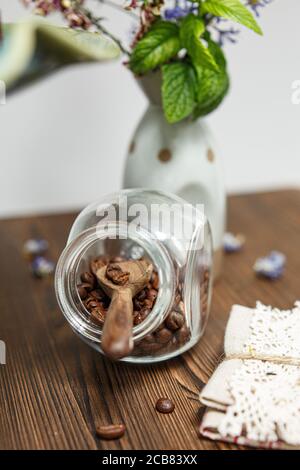 Glas gefüllt mit gerösteten Kaffeebohnen neben einem Blumenvase Stockfoto