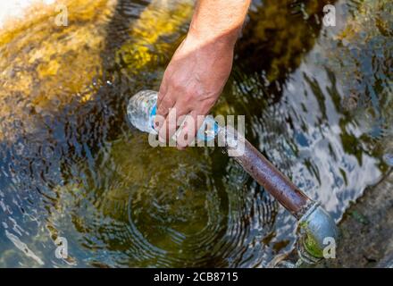 Draufsicht auf das Füllen der Plastikflasche mit Wasser aus dem Brunnen Stockfoto