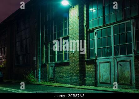 Eine Industriefassade mit alten Türen in der Nacht, alte Tore mit Glas, eine Industriefassade in der Nacht Stockfoto