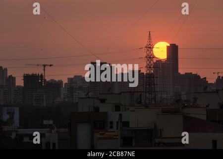 Mumbai, Maharashtra, Indien - März 2020: Panoramablick auf einen Sonnenuntergang hinter einem elektrischen Mast und eine Skyline von hohen Wolkenkratzern im Vorort Kandivali Stockfoto