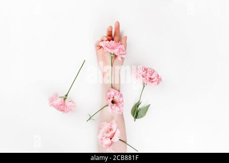 Eine zarte weibliche Hand, auf der sich Blumen von rosa eustoma befinden. Weißer Hintergrund. Flach liegend. Speicherplatz kopieren. Das Konzept der Floristik und Zärtlichkeit. Stockfoto