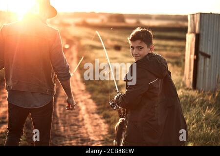 Vater und Sohn nahmen Angelruten und Angelausrüstung. Sie gehen auf Landstraße in der Nähe des Sees zum Angeln Stockfoto