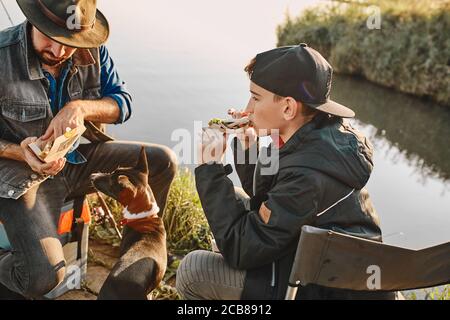 Teen junge isst die meisten leckeren Sandwich in der Natur. Er ist hungrig nach langem Fischen, er hat guten Fang. Stockfoto