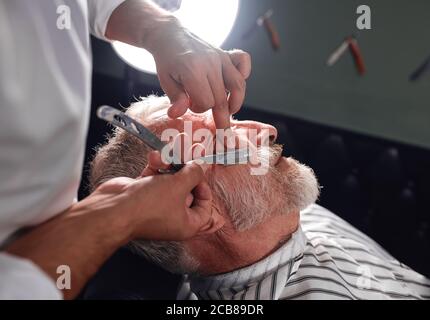 Stylist berührt den Check seines Kunden mit dem Finger, rasieren Gesichtshaare, Nahaufnahme abgeschnitten Seitenansicht Foto Stockfoto