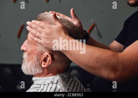 Friseursalon mit alten Männerhaaren im Friseursalon, Nahaufnahme von der Seitenansicht, Männerhand, die die Haare des älteren Mannes berührt Stockfoto