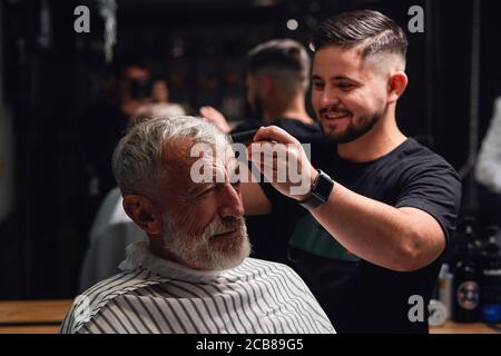 Lächelnd ehrfürchtig junge Barbier Bürsten die Haare von älteren Mann, Vorbereitung auf Haare schneiden Stockfoto