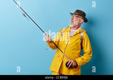 Verrückt lustig lächelnd alten Fischmann genießen Hobby, Nahaufnahme Foto. Isoliert blauen Hintergrund, kopieren Raum, Glück Stockfoto