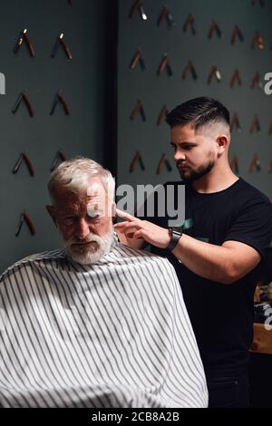 Junger Mann trimmt Haare des alten Mannes über den Ohren. Nahaufnahme. Stockfoto