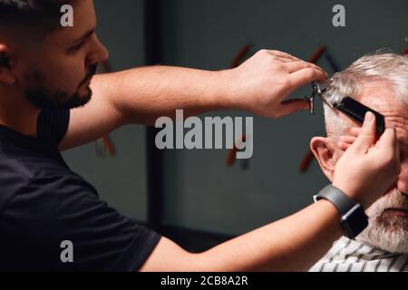 Junge talentierte Barbier tun neue moderne Frisur für Kunden. Barbier Vorbereitung alter Mann für ein Datum, Partei, Ereignis Stockfoto